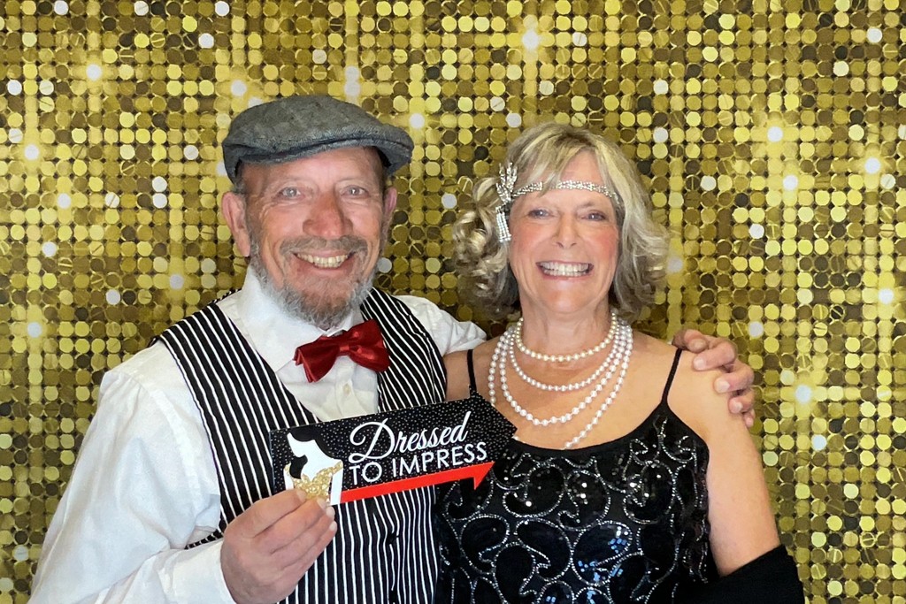 Couple in 1920s outfits smiling at a trivia night photo booth