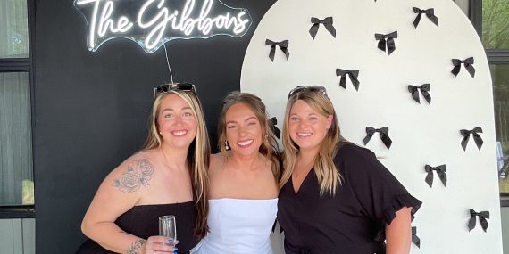 Guests smiling in front of InstaGlee's chiara arch backdrop walls with a custom neon sign at a wedding shower
