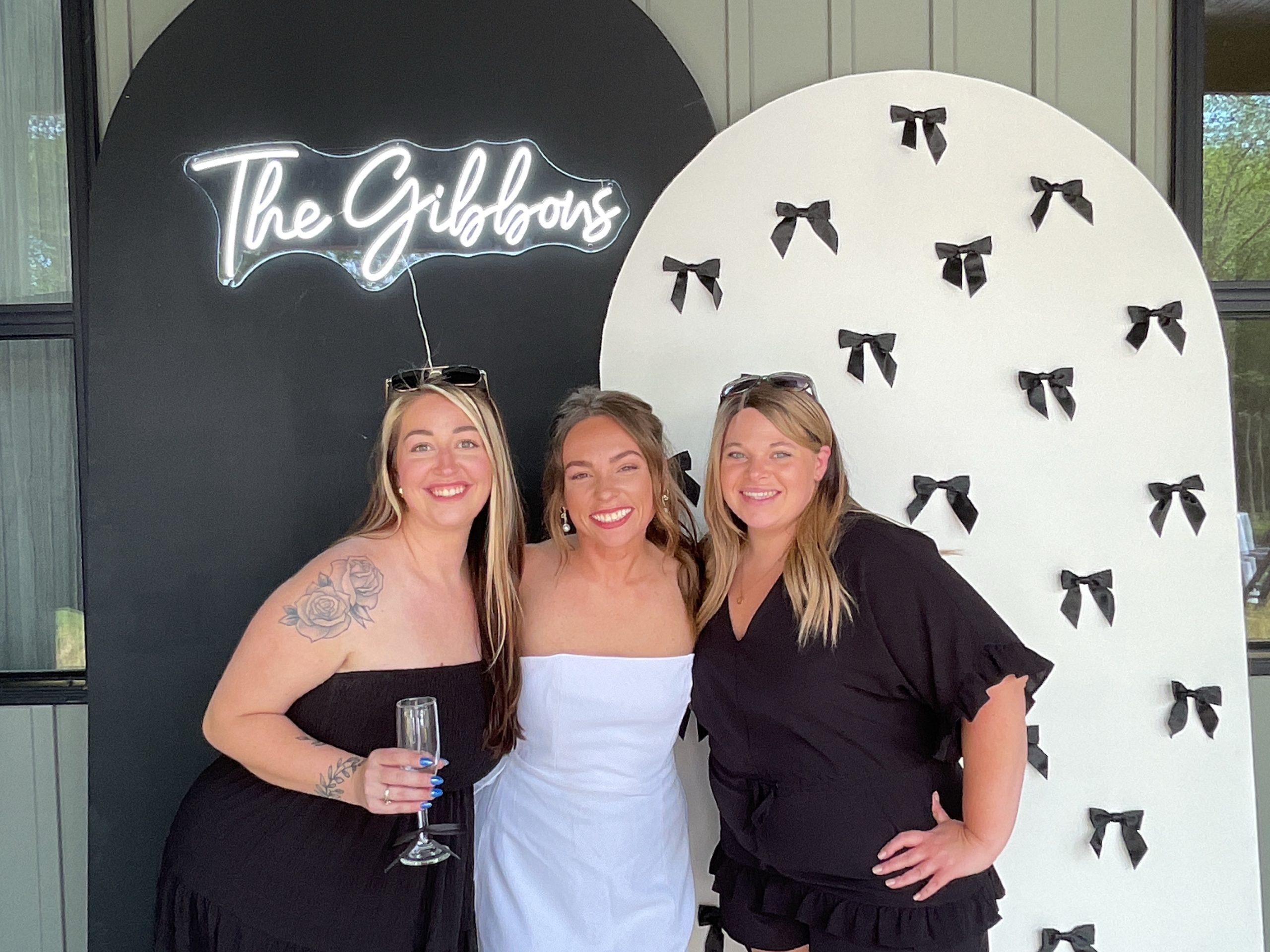 Guests smiling in front of InstaGlee's chiara arch backdrop walls with a custom neon sign at a wedding shower