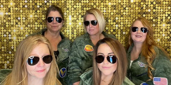 A trivia team in matching flight suits and aviator sunglasses posing in front of InstaGlee's gold sequin backdrop